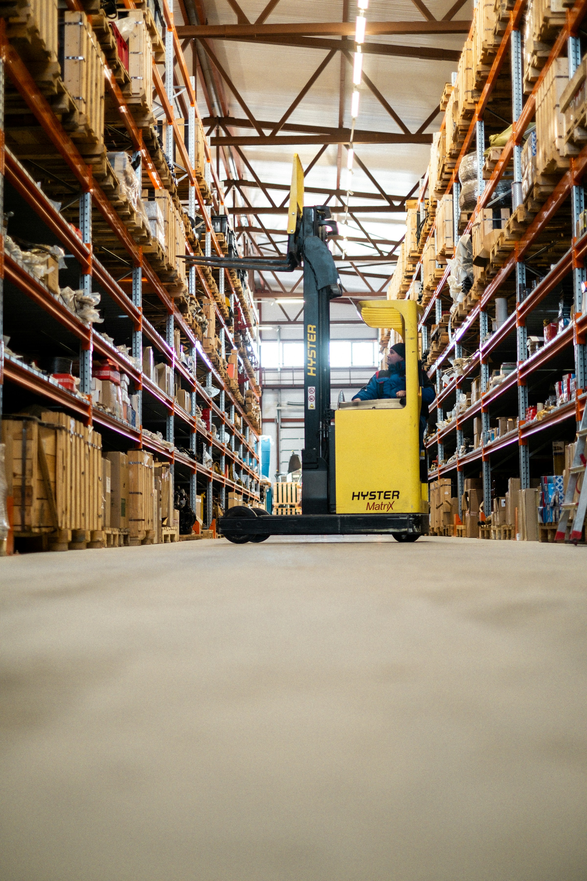 Warehouse worker operating lift equipment between tall storage racks